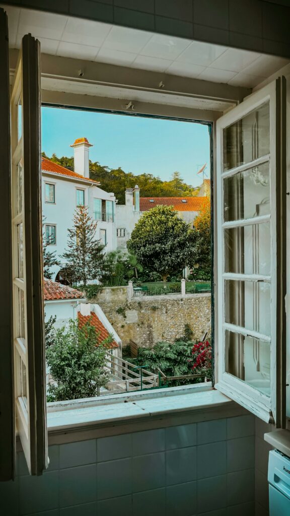 View of charming architecture and nature through an open window, capturing a peaceful neighborhood ambiance.